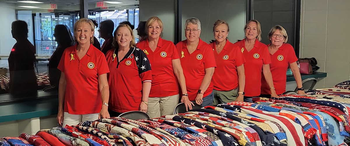 women of the Post 484 Auxiliary standing behind a table covered in quilts