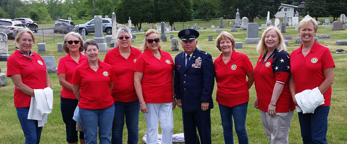 women of the Post 484 auxiliary posing with a male military veteran at a cemetary